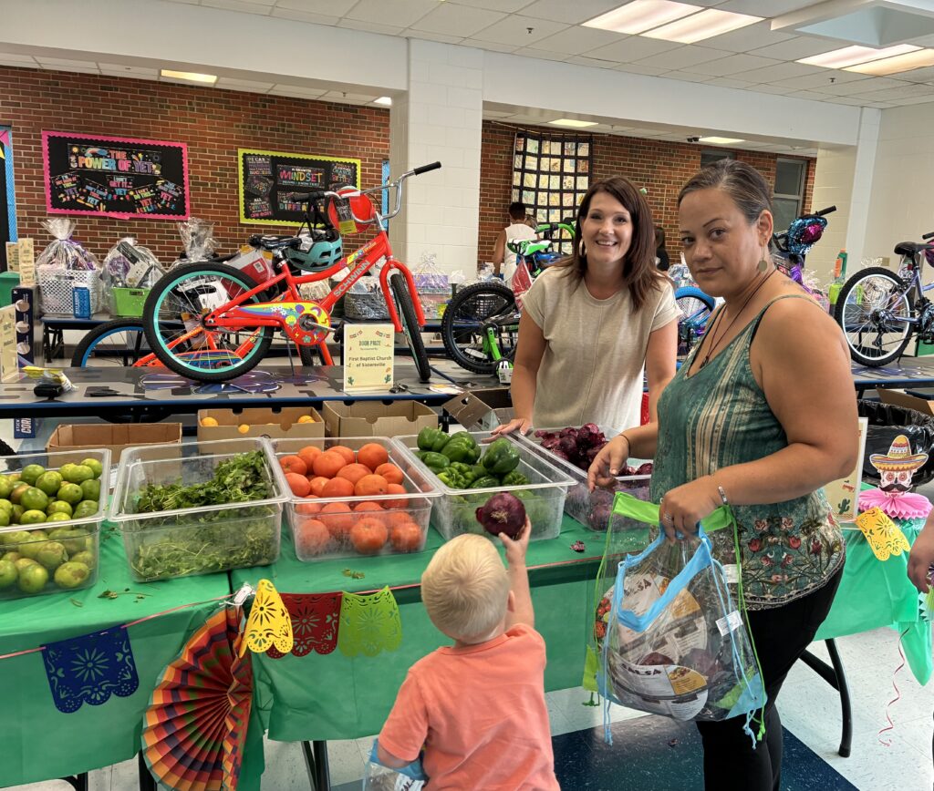 Two women and a child at a vibrant indoor table with fresh vegetables and decorative details. Brightly colored bikes in the background add a playful touch.